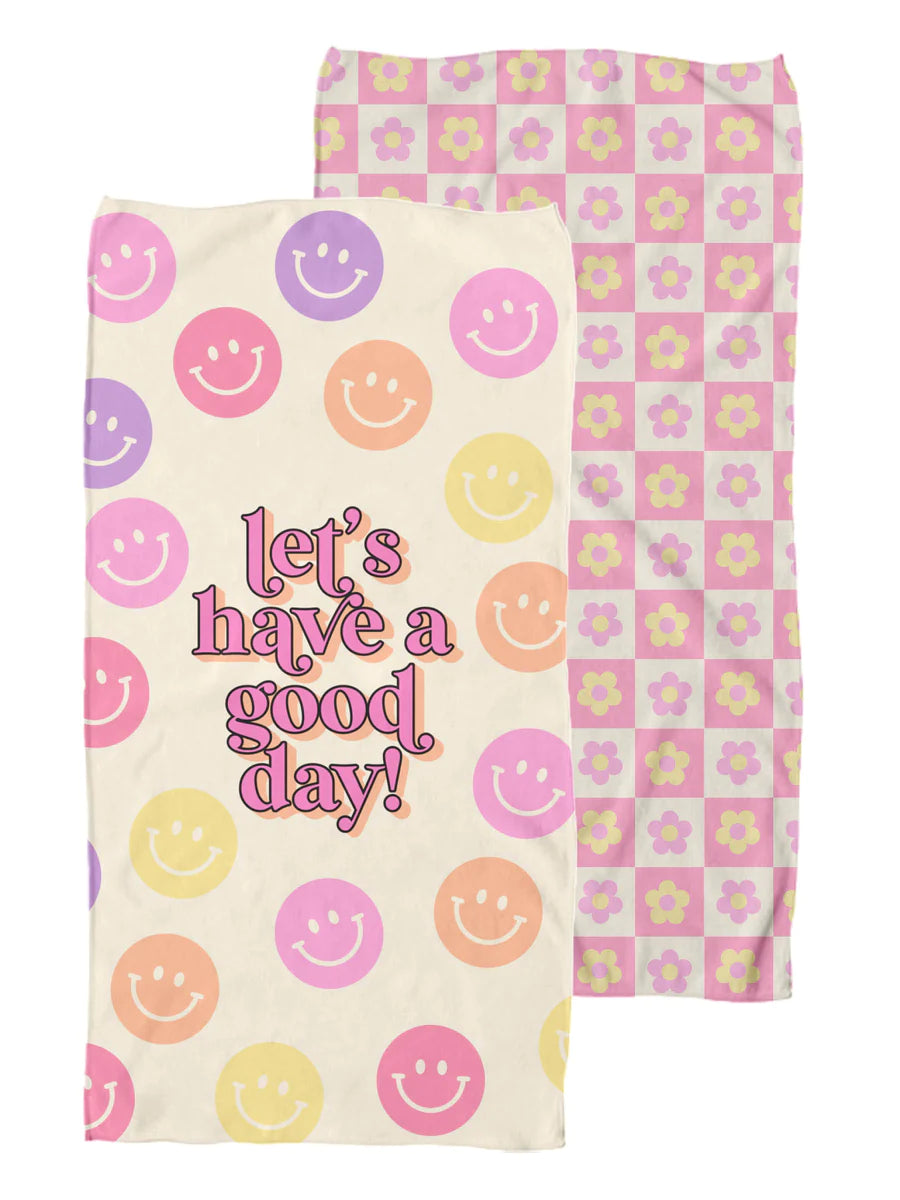 two sided towel. one side is a yellow base with smiley faces and "lets have a good day!" scripted in pink. The other side is pink and white checkered with pink and yellow flowers.