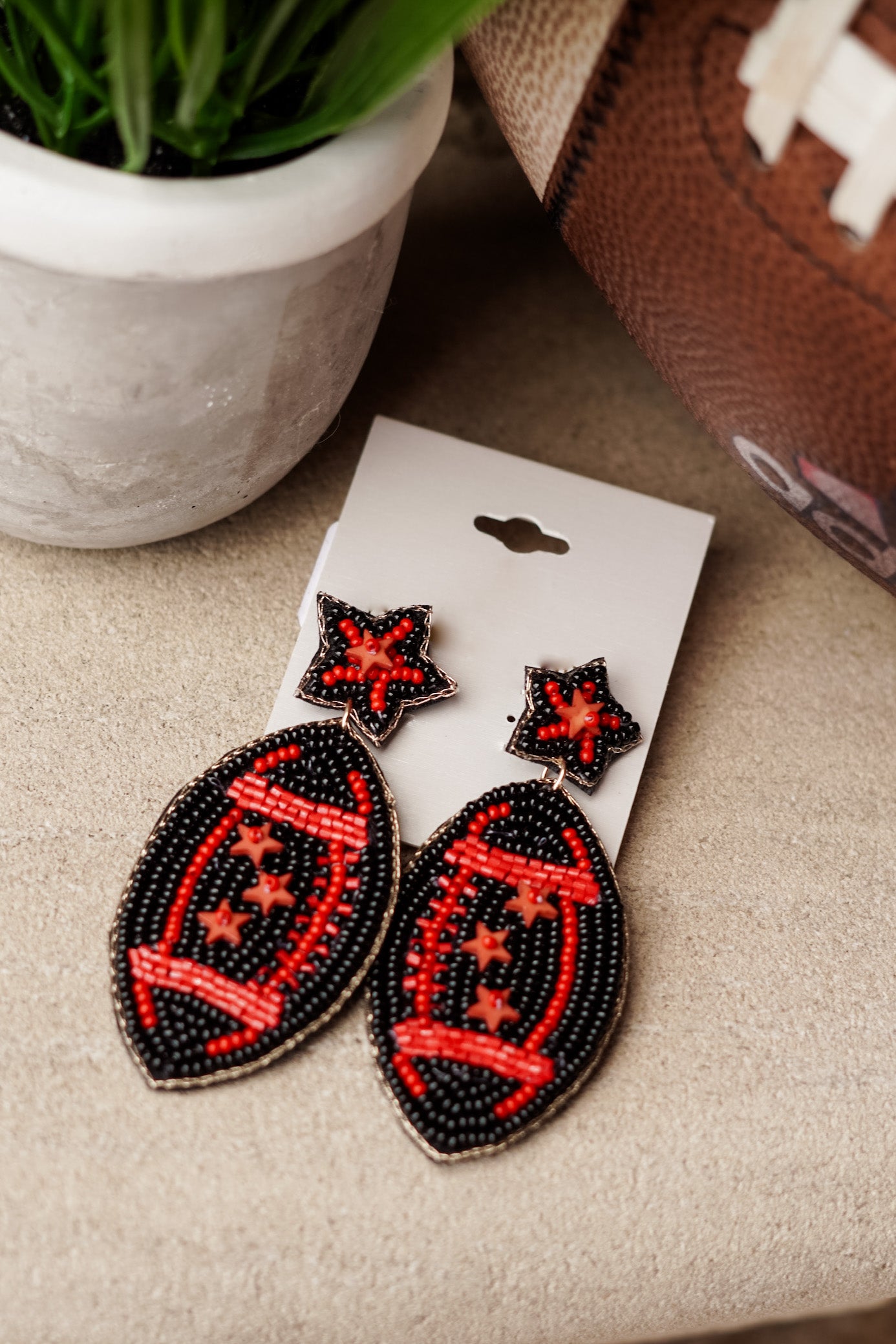 Red and black, Red and Black!! For all the red and black teams out there, these Snap The Ball Beaded Earrings will be your favorite accessory under the Friday or Saturday Night Lights!! Snap The Ball Beaded Earrings Football and Stars Stud Post Back. Red and black beaded football earrings, black background with red outline and red stars.