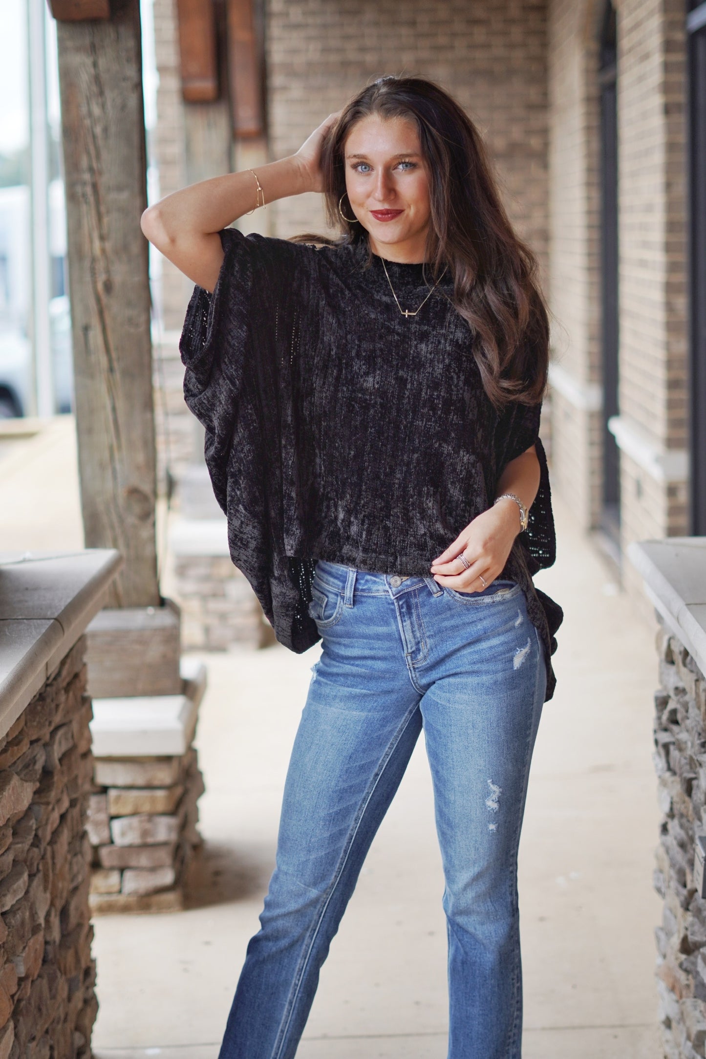 Sherry Chenille Sweater Top Round Neckline Angel Wing Sleeve Chenille Fabric Black Color Relaxed Fit Full Length. Brunette model, jeans, stone and brick background.
