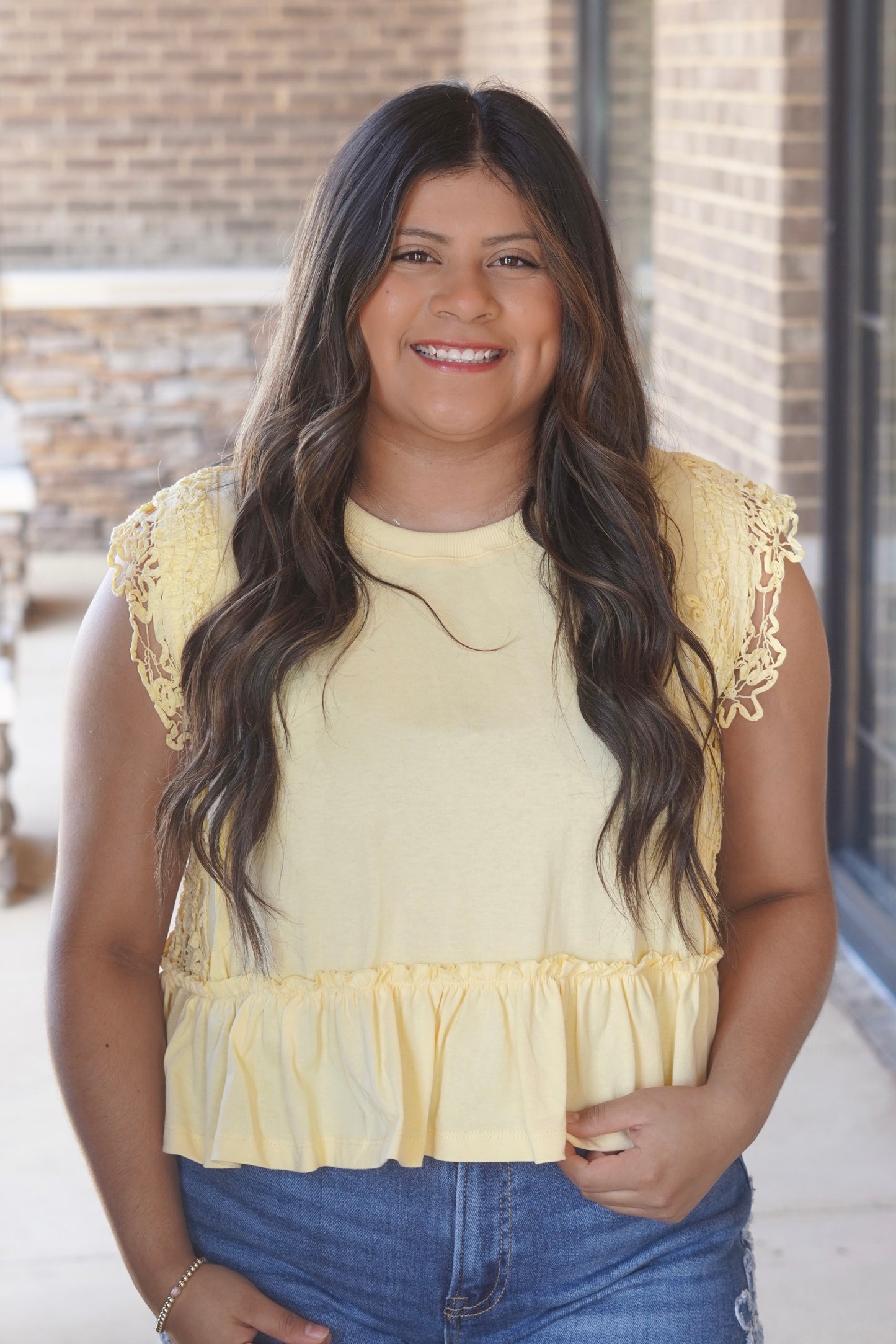 Women wearing a yellow top with a ruffle hem and lace on the side of the top.