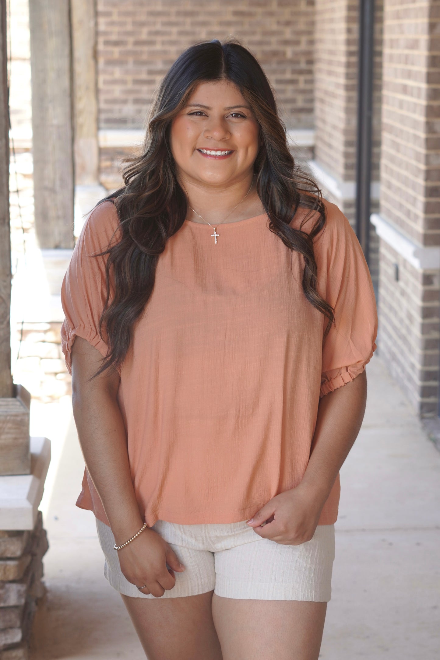 Women wearing an apricot color blouse, with elastic sleeves, round neckline, styles with tan shorts.