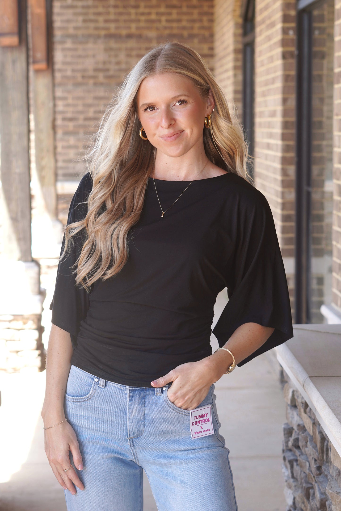 Woman wearing a black top, with cinch waist and mid-length flowy sleeves and white pants