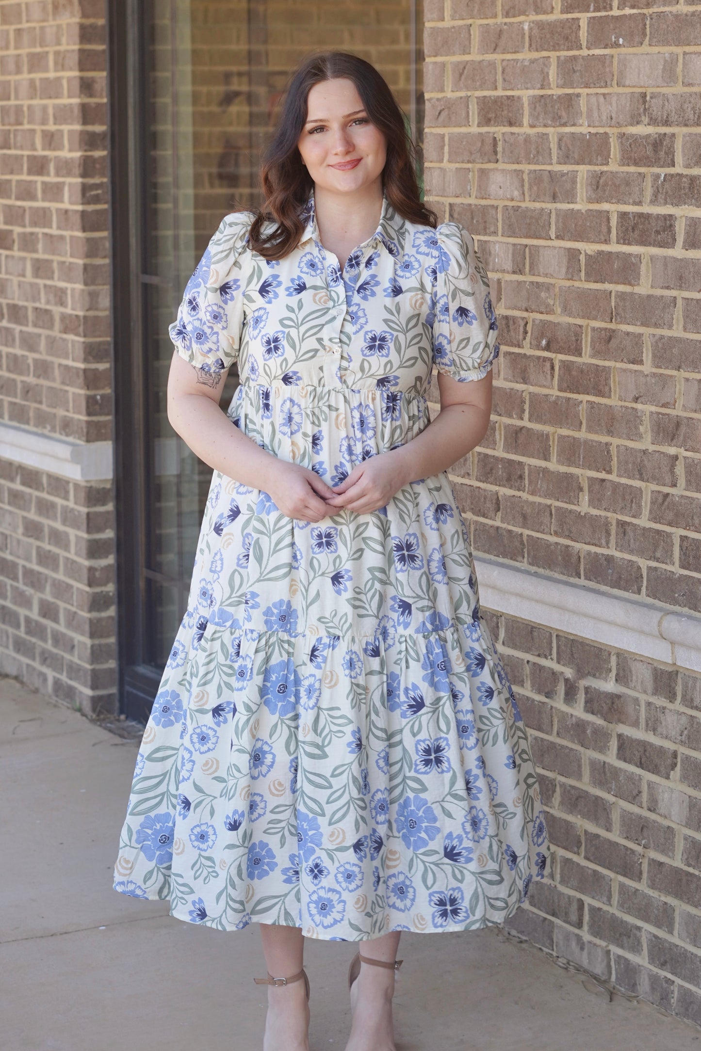Woman wearing a blue and green floral, short puff sleeve, collared maxi dress paired with nude heels.