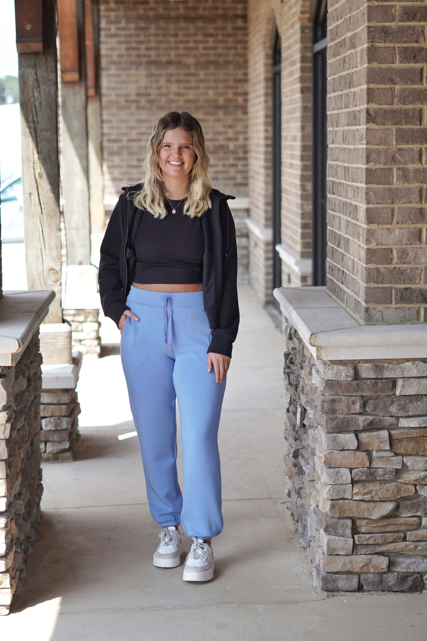 Model wearing Spanx Air Essentials Blue Joggers With Black Shirt and Black Jacket and Sneakers