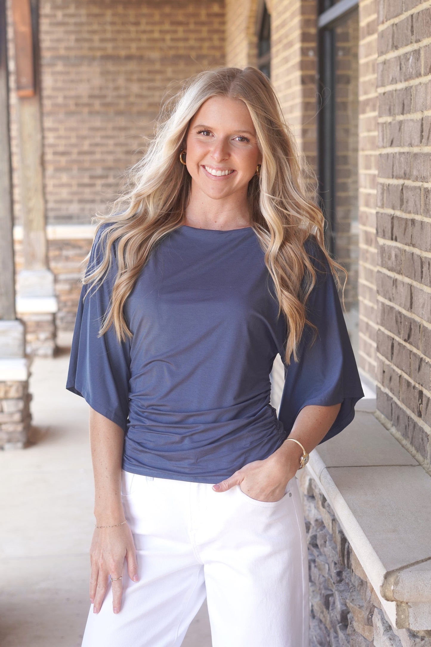 Woman wearing a blue top, with cinch waist and mid-length flowy sleeves and white pants