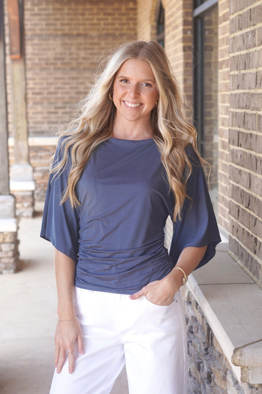 Woman wearing a blue top, with cinch waist and mid-length flowy sleeves and white pants