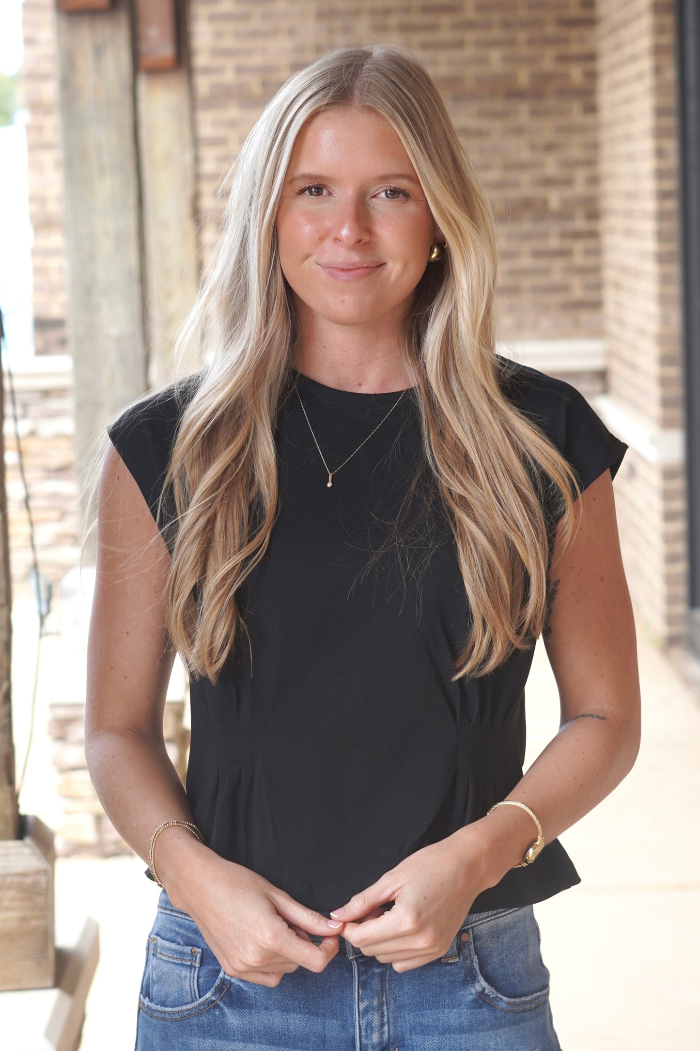women wearing a black cap sleeve top, round necklines, and snitch detail.