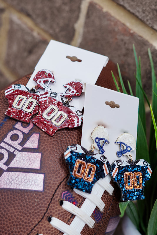 Friday Night Lights are upon us!! Whether you have a son or boyfriend on the field, or you're watching on the Big Screen TV in your living room, represent your team with the "Gear Up" Jersey Earrings!! "Gear Up" Jersey Earrings Crimson/White and Navy/Orange Stud Post Back. Red/white sequin jersey with football helmet on the post. Navy/orange sequin jersey with football helmet on the post.