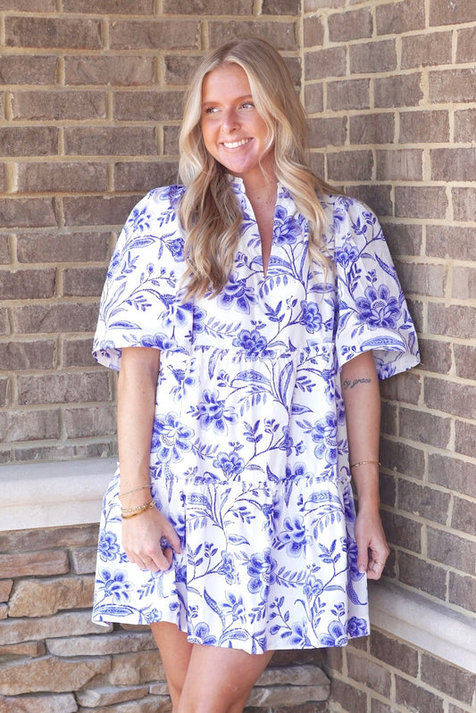 White tiered dress with royal blue floral and paisley print. Short sleeve. V-neckline. Hits above the knee.
