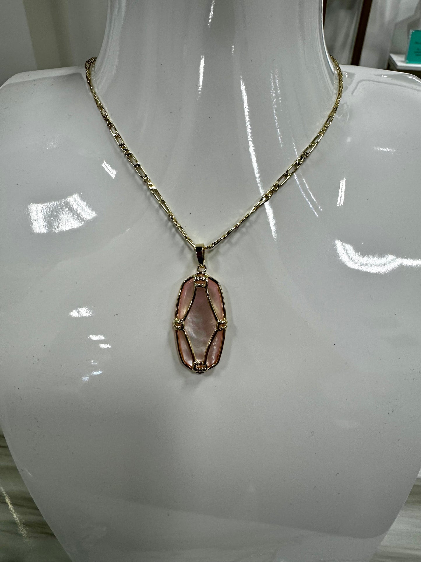 gold necklace featuring an oval, light pink pendant encased in a decorative gold wire .