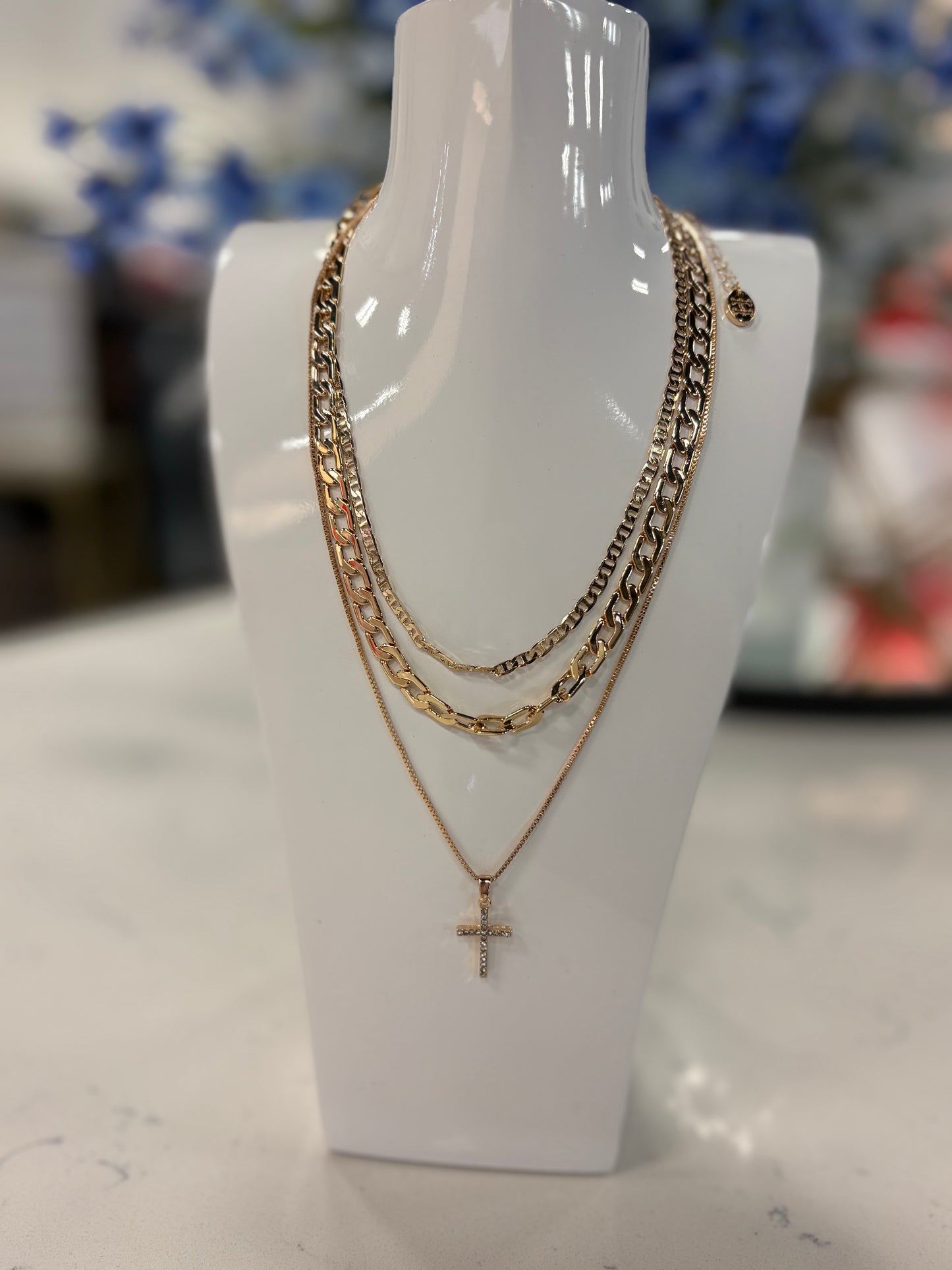 Beautiful, layered gold necklace set. It feature three chains styles, including two classic curb chains, both of different sizes and a delicates chain with a rhinestone cross pendant.