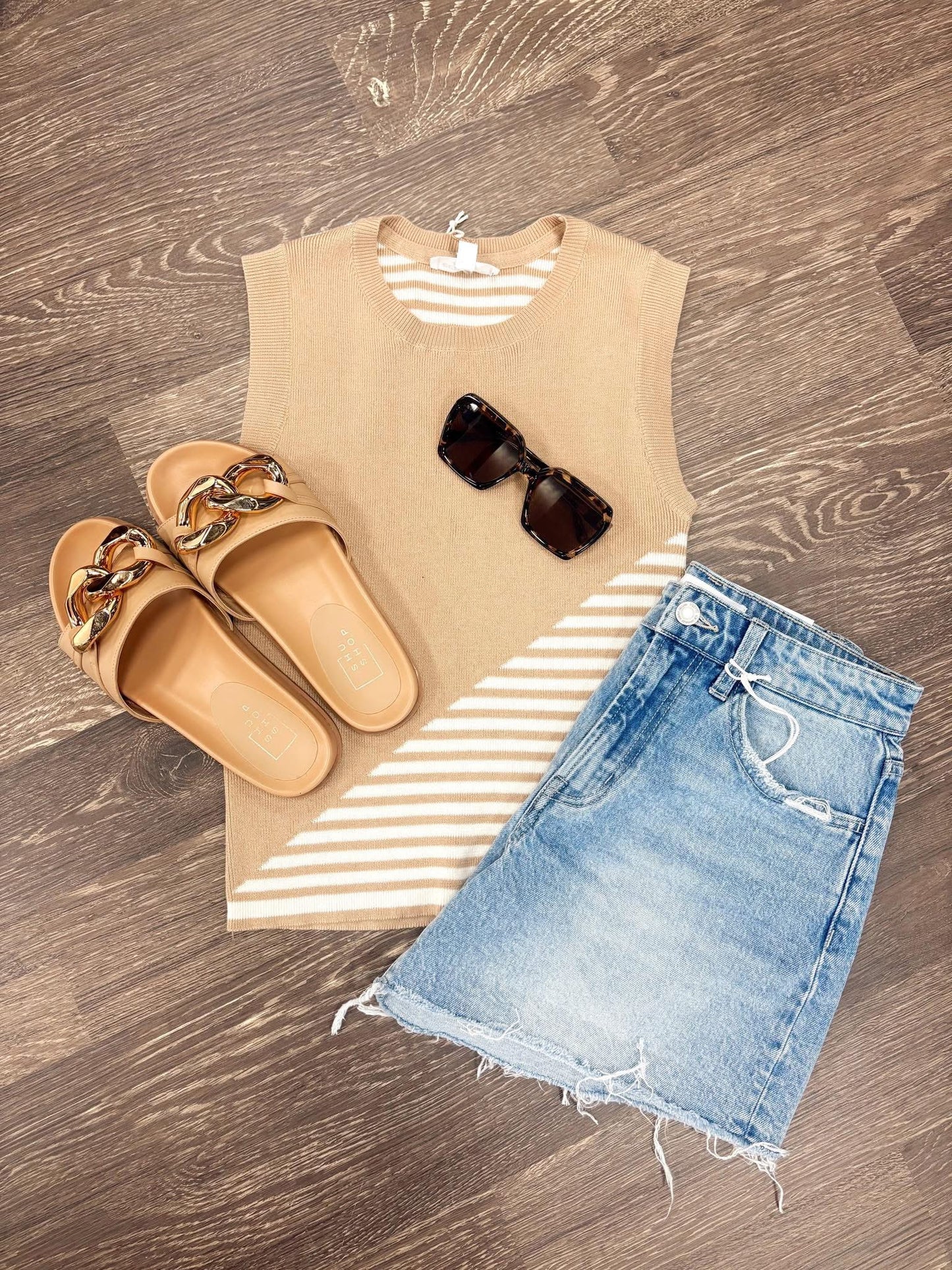 A flat lay of a taupe tank top with white strip on the side, a pair of jean shorts, sunglass and some tan color sandals.