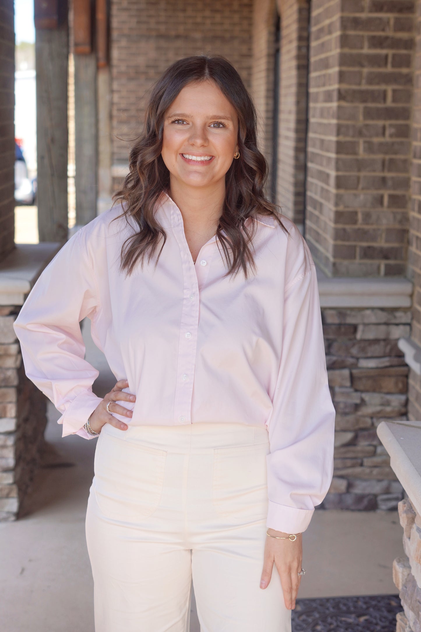 Women wearing a light pink long sleeve button up top, paired with some white pants.