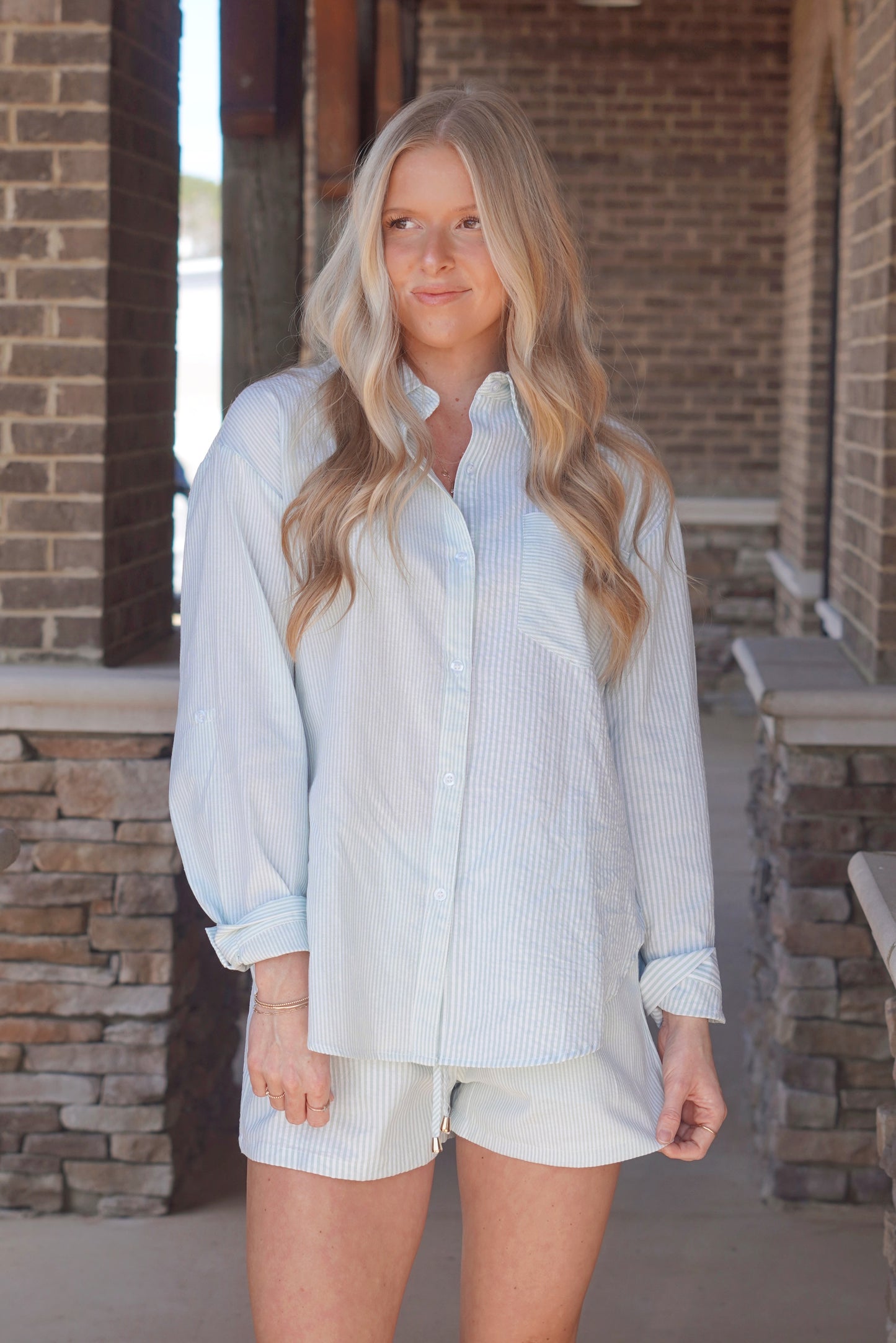 Women wearing a sage stripe long sleeve button up top with a collar neckline, paired with matching shorts.