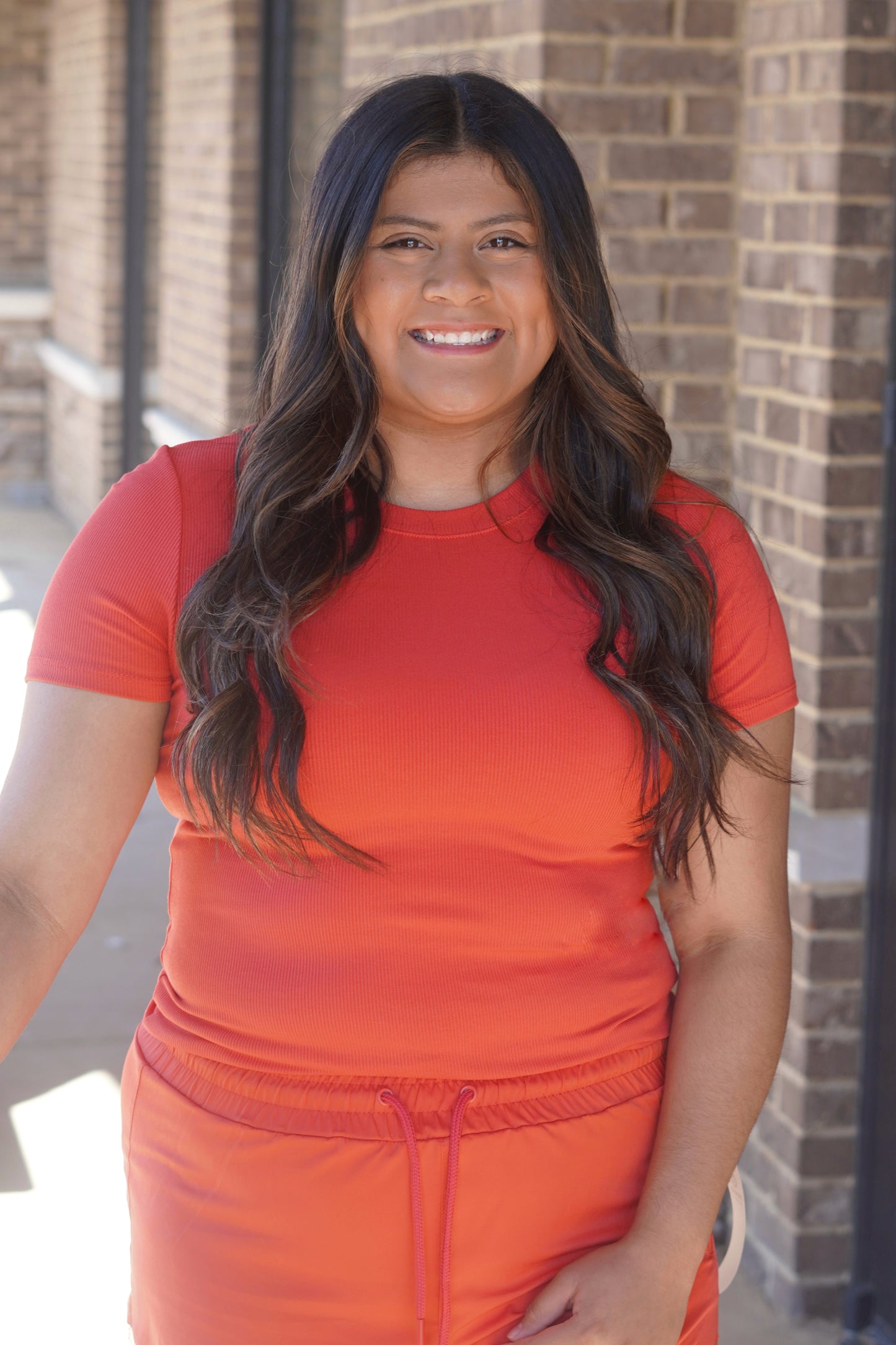 Women wearing an orange fitted short sleeve shirt with micro ribbing, a rounded neckline.