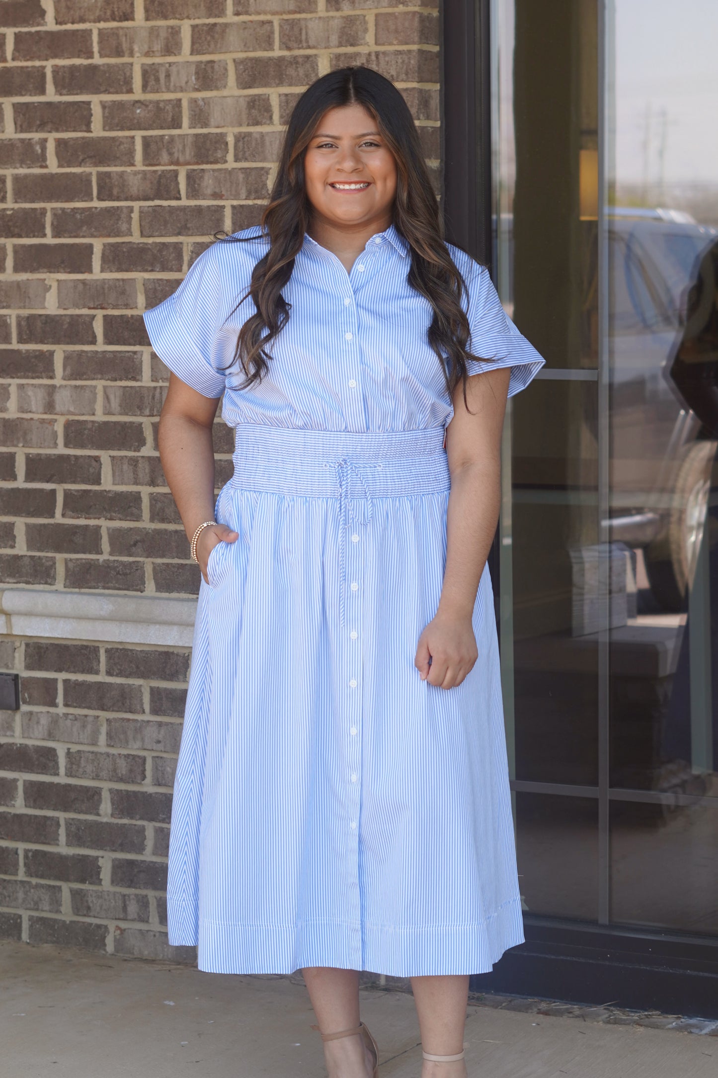 Women wearing a blue and white stripes midi dress, button up style, elastic waistband, with shorts sleeves.