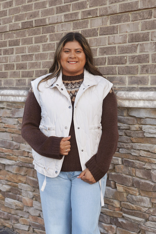 Women wearing an ivory Bow Detail Quilted Puffer Vest, Collar Neckline, Snap Button Down, Full Length, Pockets, Style with a brown sweater and jeans.