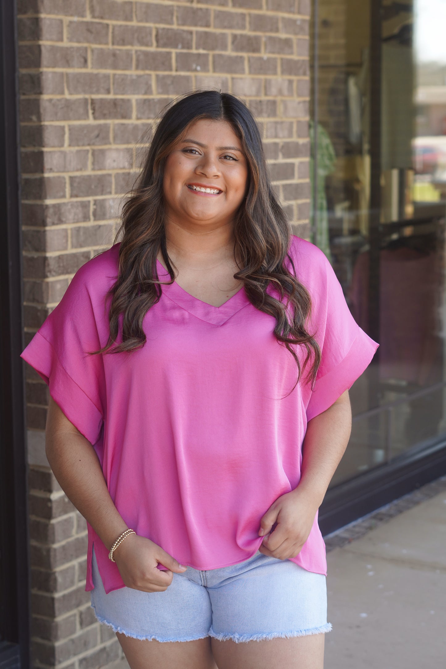 Woman wearing a pink v-neck top, short sleeve, flowy, paired with light blue jean shorts