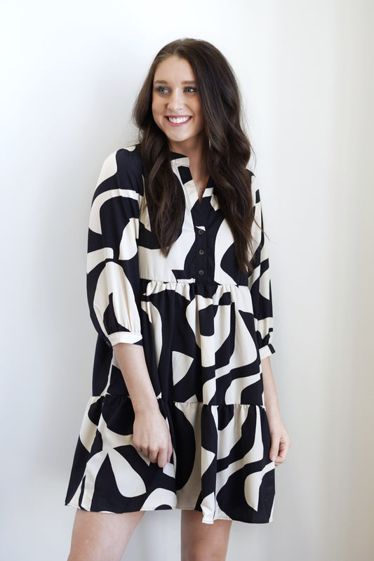 Adeline Abstract Button Down Dress Button Down Neckline Half Sleeves Tiered Ruffle Detail Colors: Black and Taupe Abstract Swirl Print Knee Length 100% Polyester