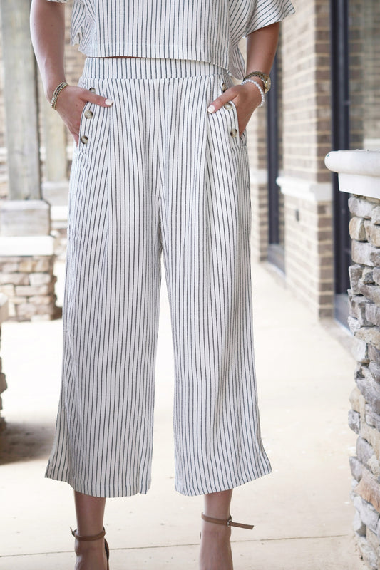 Sonny Striped Cropped Pants High Waisted Wide Leg Pockets Lined w/ Buttons Color: Off White w/ Black Pinstripes Relaxed Fit Cropped Leg Length 70% Viscose, 30% Linen
