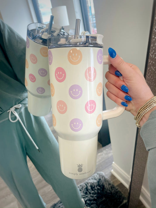 cream colored tumbler with a handle and orange, pink, and purple smiley faces