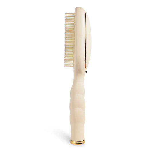 Side view of a oval beige hairbrush with an textured handle and gold trim.