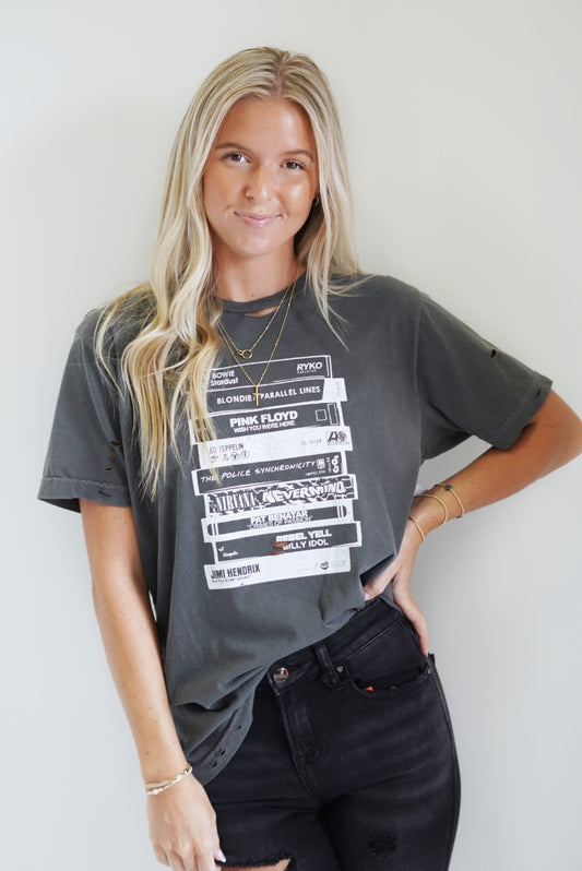 Maeva Music Lover Graphic Tee Crew Neckline Short Sleeve Distressed T-Shirt Stacked Tapes on front of shirt Dark Grey True to size Sizes medium-XXL Model is wearing size: 100% Cotton Machine wash warm, inside out with like colors Model is wearing a size medium