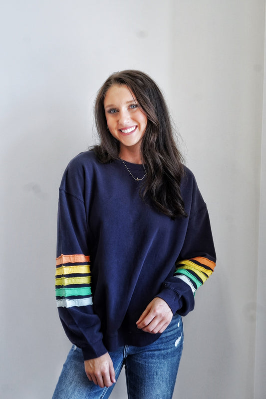 Sadie Striped Sleeve Crew Neck Crew Neckline Long Cuffed Sleeves Colorful Stripes on Sleeve Base Color: Navy Stripe Colors: Orange, Yellow, Green, White Relaxed Fit Full Length 100% Cotton