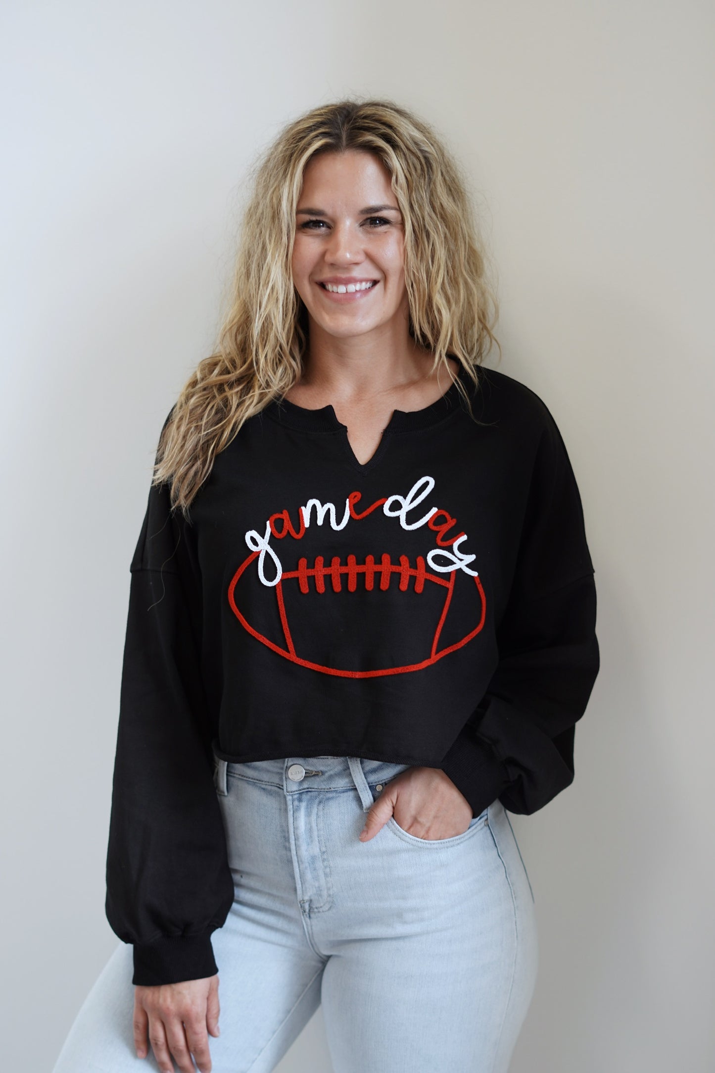 Gwen "Game Day" Cropped Crewneck Top Crew Neckline w/ Slit Long Cuffed Sleeves Raw Hem Cropped Length Black with red and white lettering White Lettering Over a Football Relaxed Fit 60% Cotton, 40% Polyester Care: Hand Wash Cold, Do Not Bleach, Dry Flat