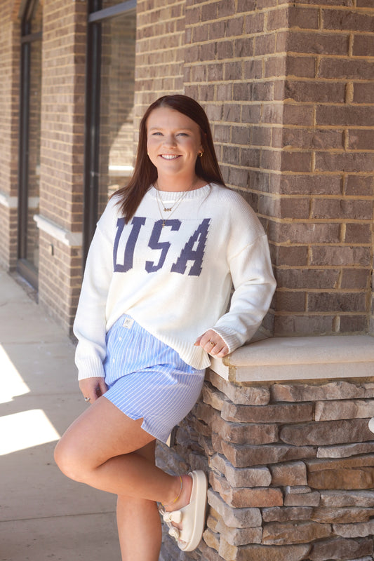 white knit sweater with blue USA printed on it, crew neck, ribbed cuffs and neckline.  