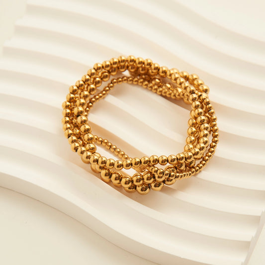 This curated 4-piece set includes four stretch-fit beaded bracelets in varying ball sizes, all finished in luminous 18K gold plating or polished Stainless Steel.