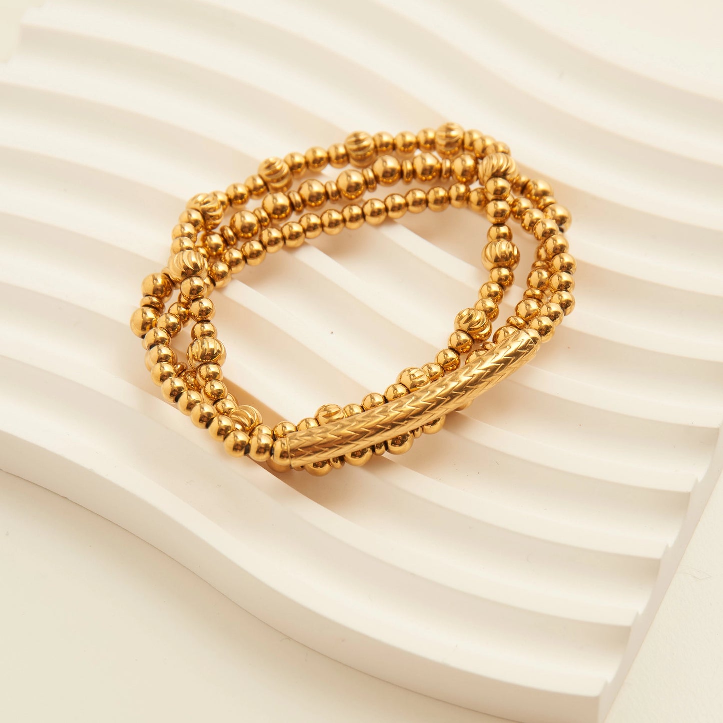 Gold multi-strand bracelet with small, round beads and a textured central bar. 