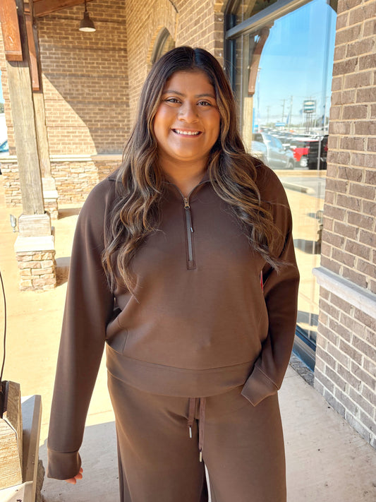 A woman wearing a matching brown lounge set consisting of a half-zip pullover and drawstring pants,