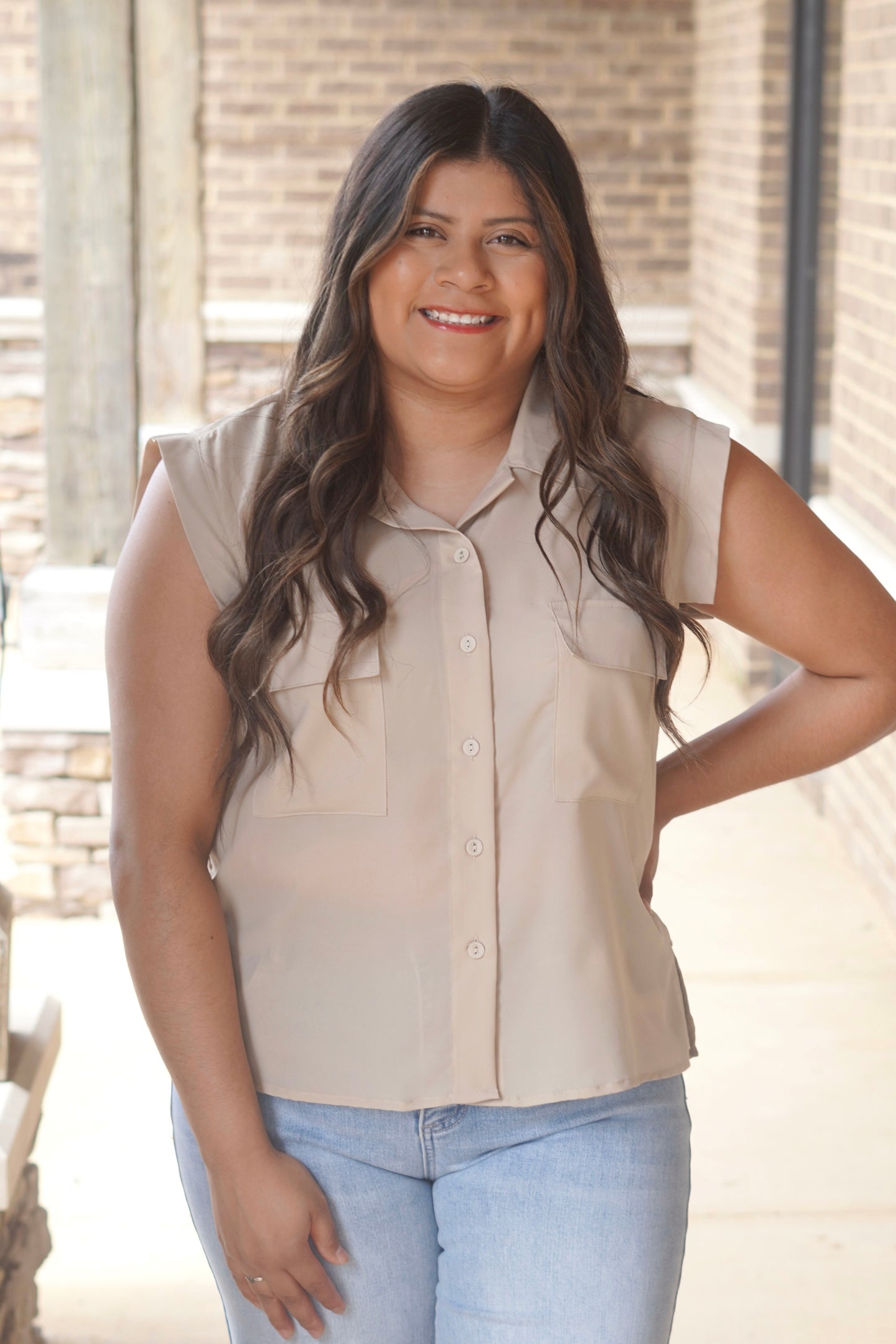 Women wearing a taupe button up top with short sleeves,  pockets in the front, collar neckline. 