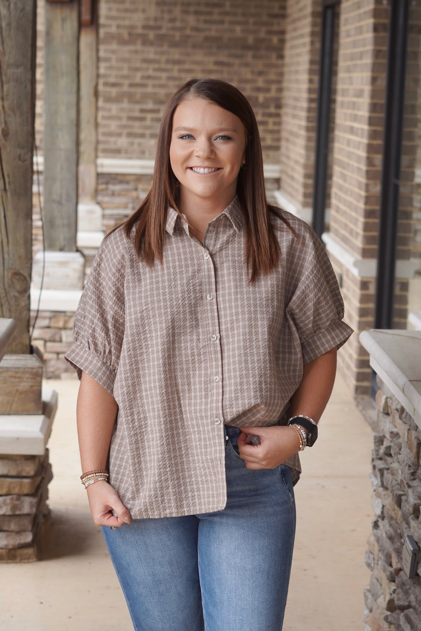 Woman wearing a brown and white short sleeve gingham button down top paired with denim jeans
