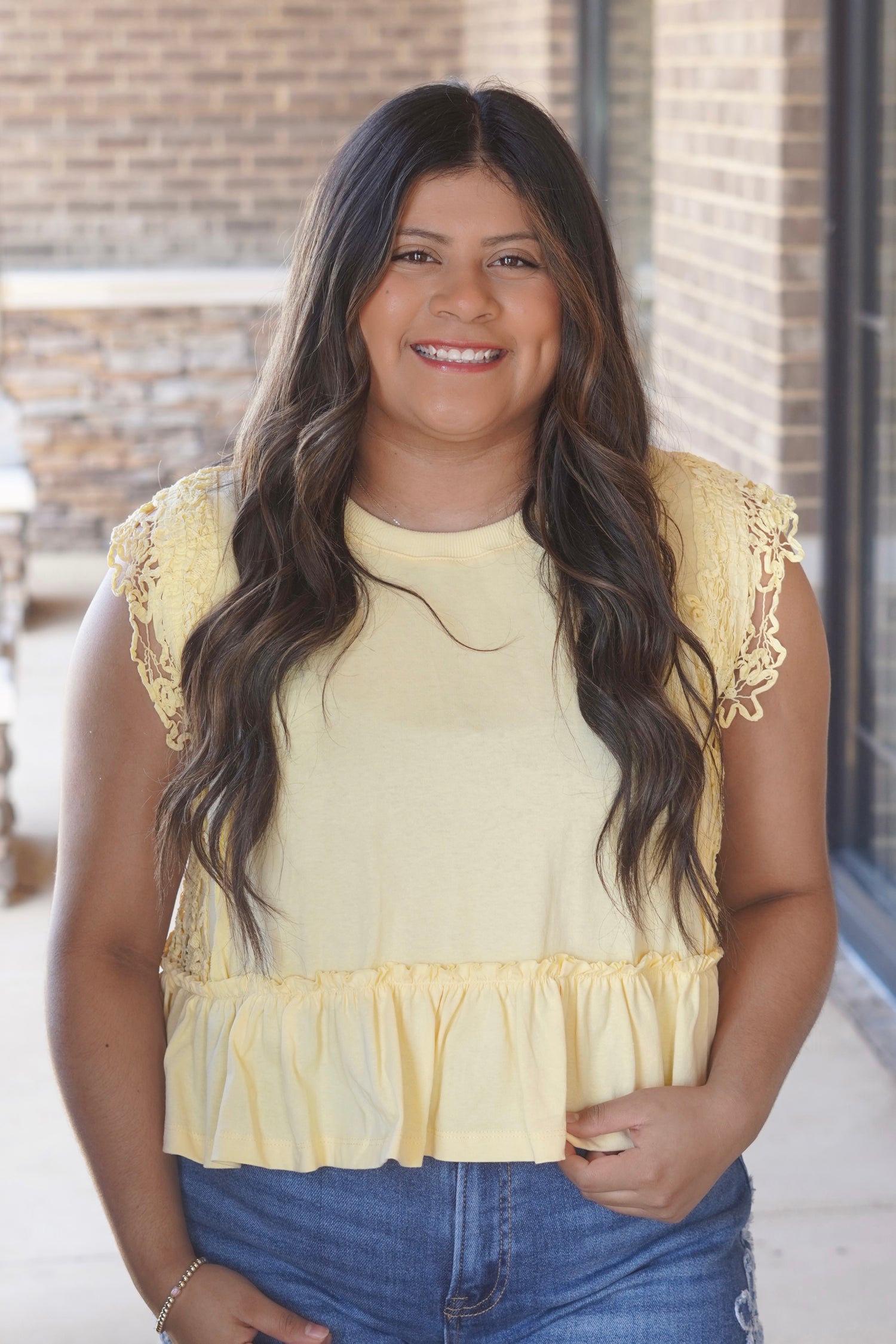 Women wearing a yellow top with a ruffle hem and lace on the side of the top. 