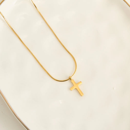A delicate gold snake chain necklace with a small, polished gold cross pendant, displayed.