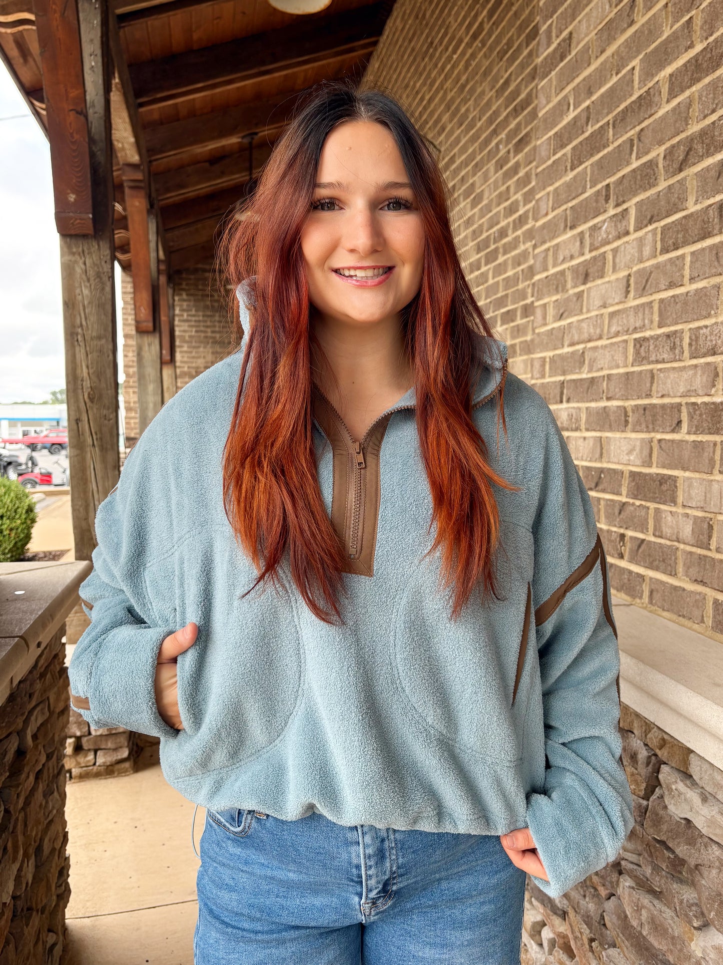 Woman wearing a blue-colored fleece quarter-zip pullover with brown stripe details on the sleeves, paired with jeans.