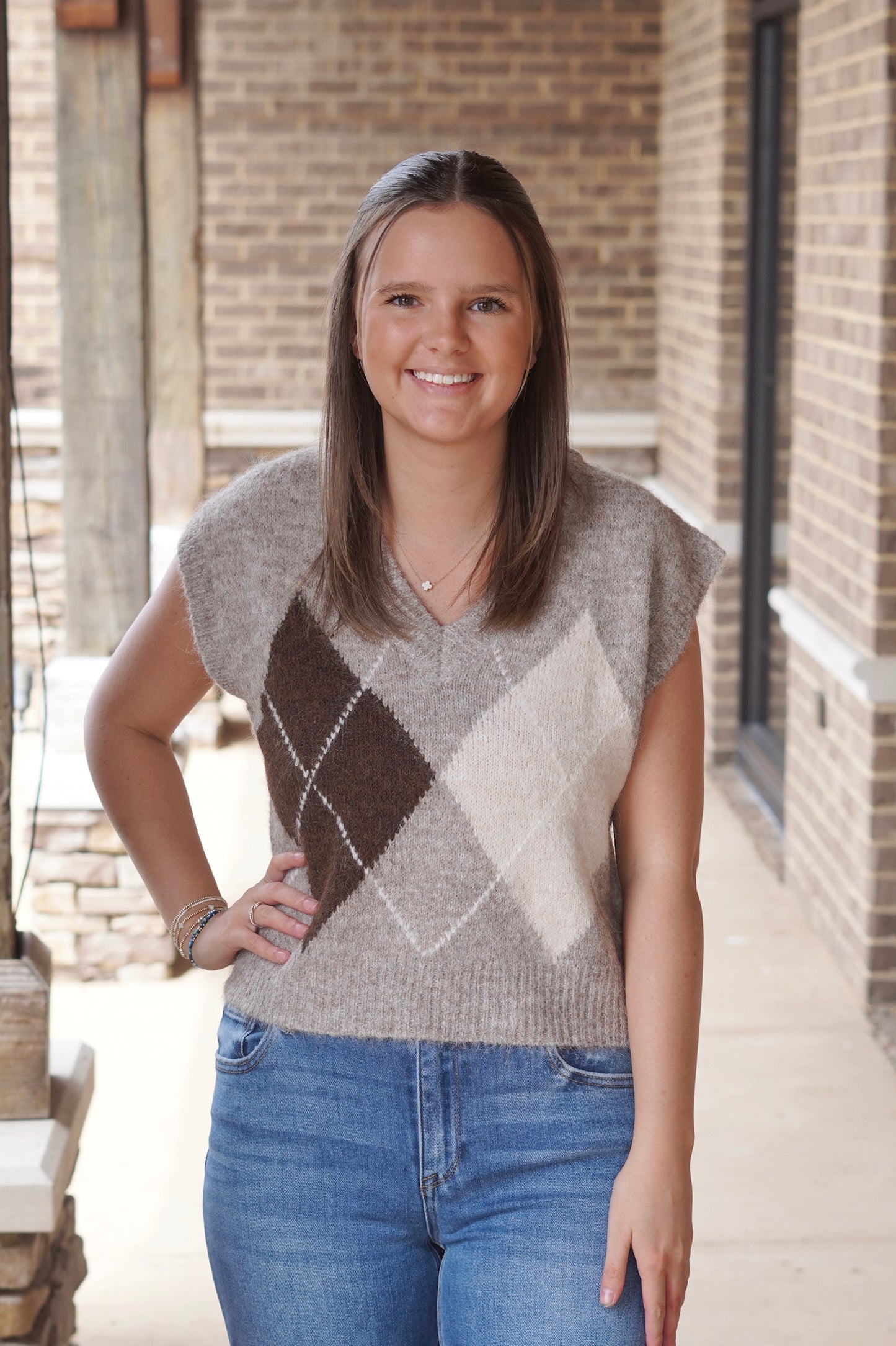 Woman wearing a brown V-Neckline Sleeveless Sweater Vest in an Argyle Pattern paired with blue jeans 