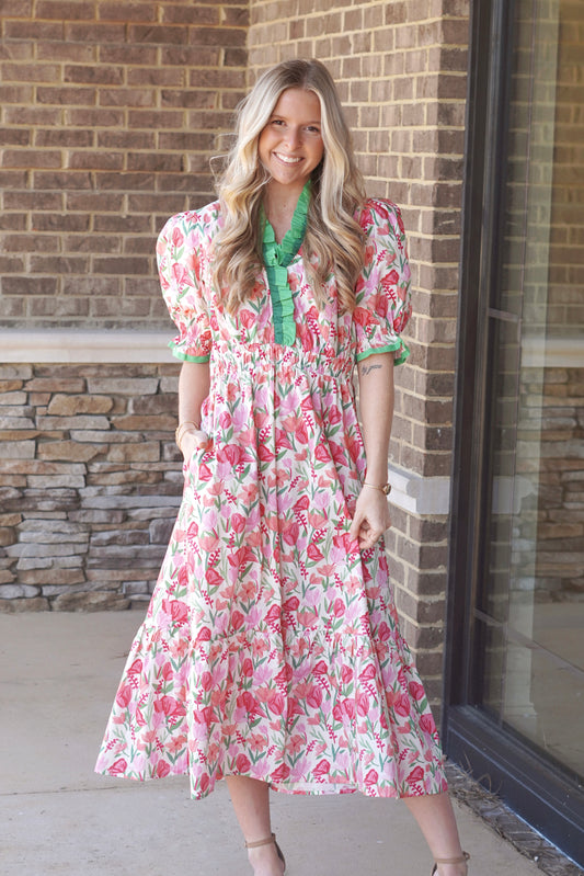 Woman wearing a pink floral maxi dress with puff sleeves and green detailing on the trim of the neckline and sleeves.