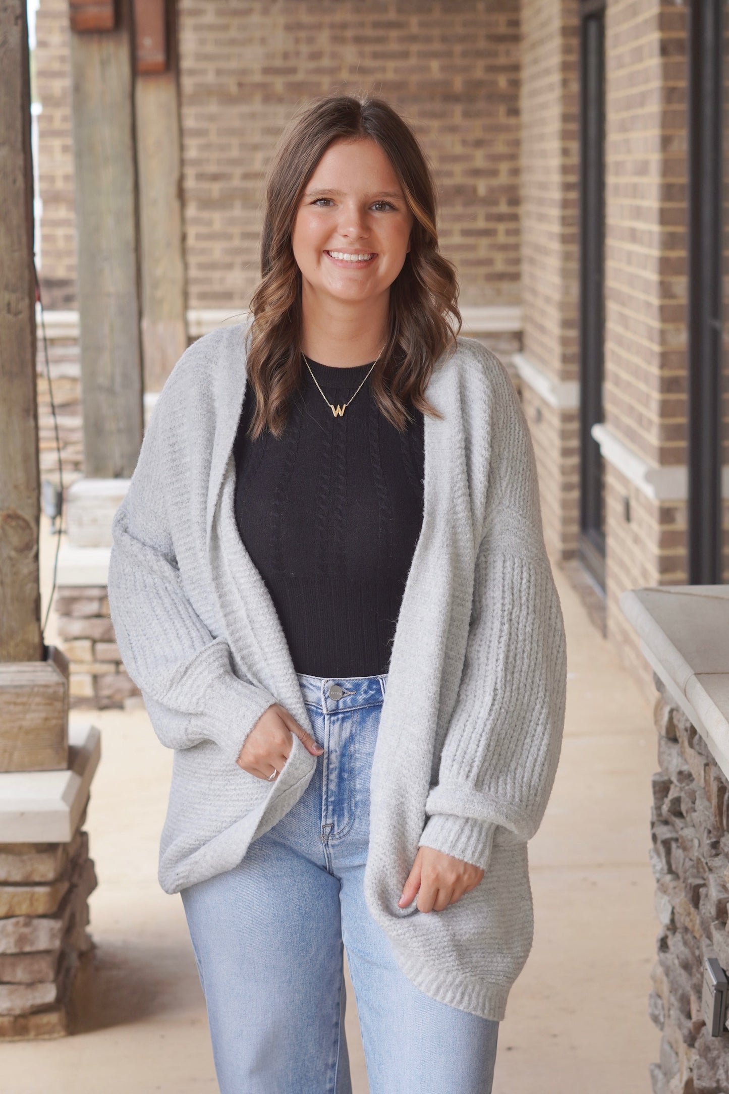 Woman wearing grey colored oversized cardigan paired with a light wash jeans and black fitted top