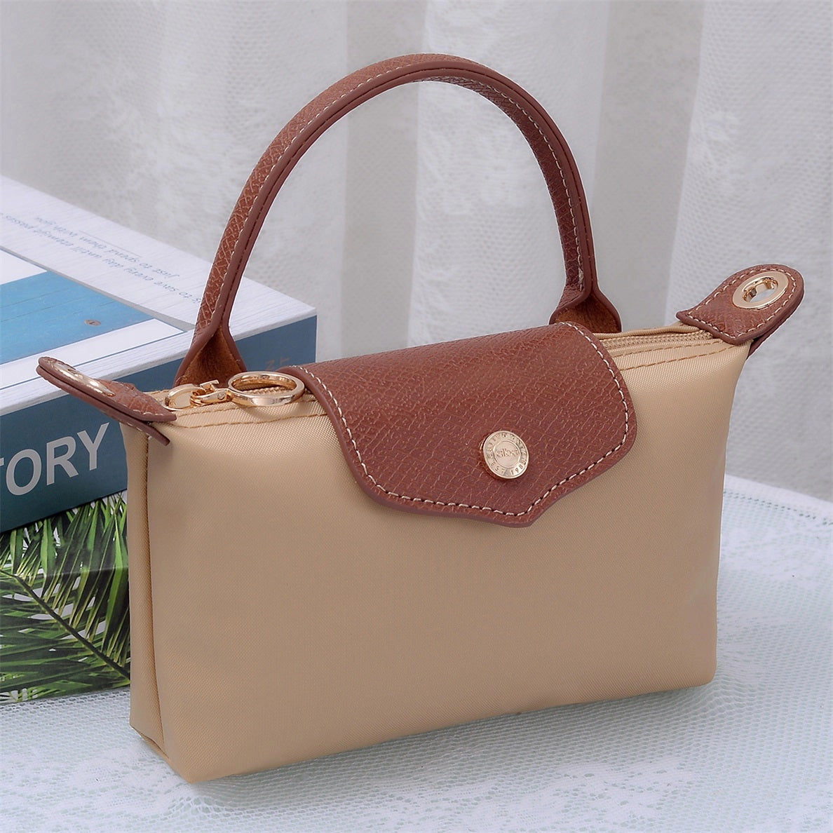 Small tan colored handbag with brown leather and gold accents 
