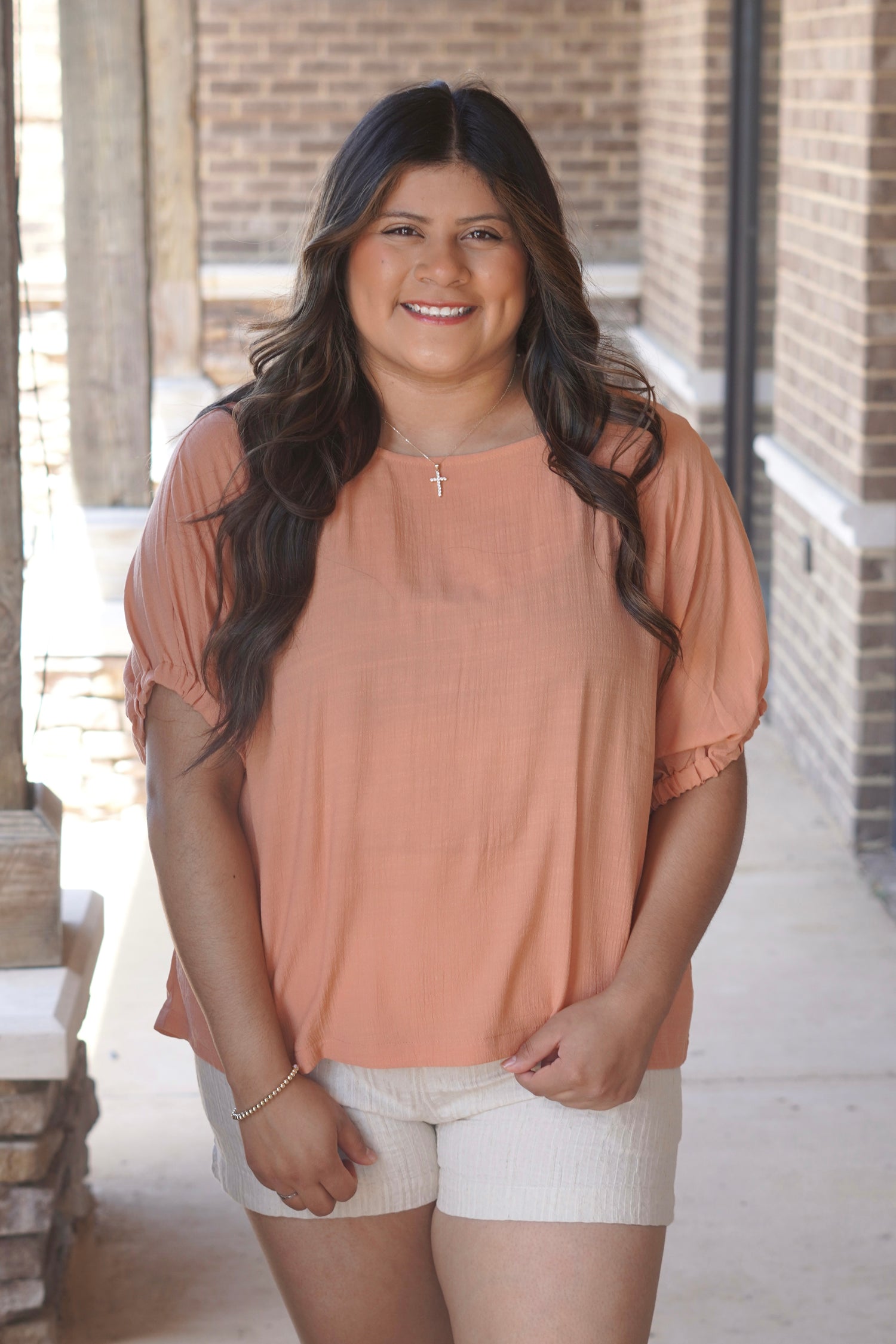 Women wearing an apricot color blouse, with elastic sleeves, round neckline,  styles with tan shorts. 