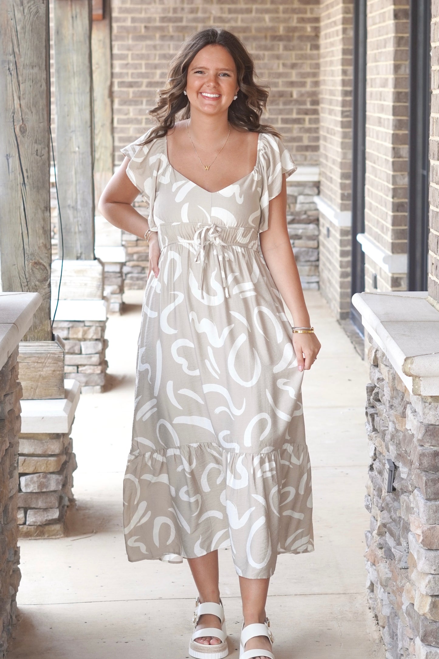 khaki colored  midi dress with a white wavy print, cinched tie waist, v-neck, and flutter sleeve