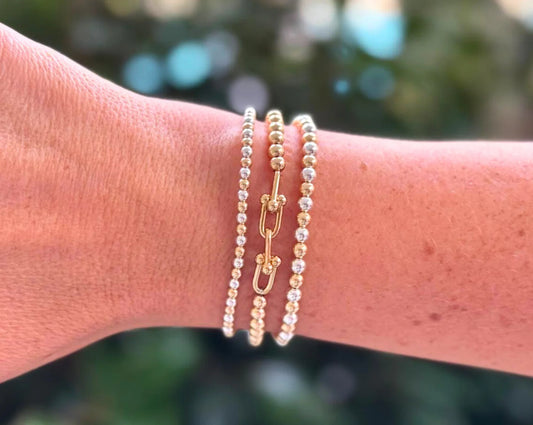 set of 3 beaded bracelets, two of the bracelets being silver and gold alternating, the third bracelet bring gold with a link attaching them