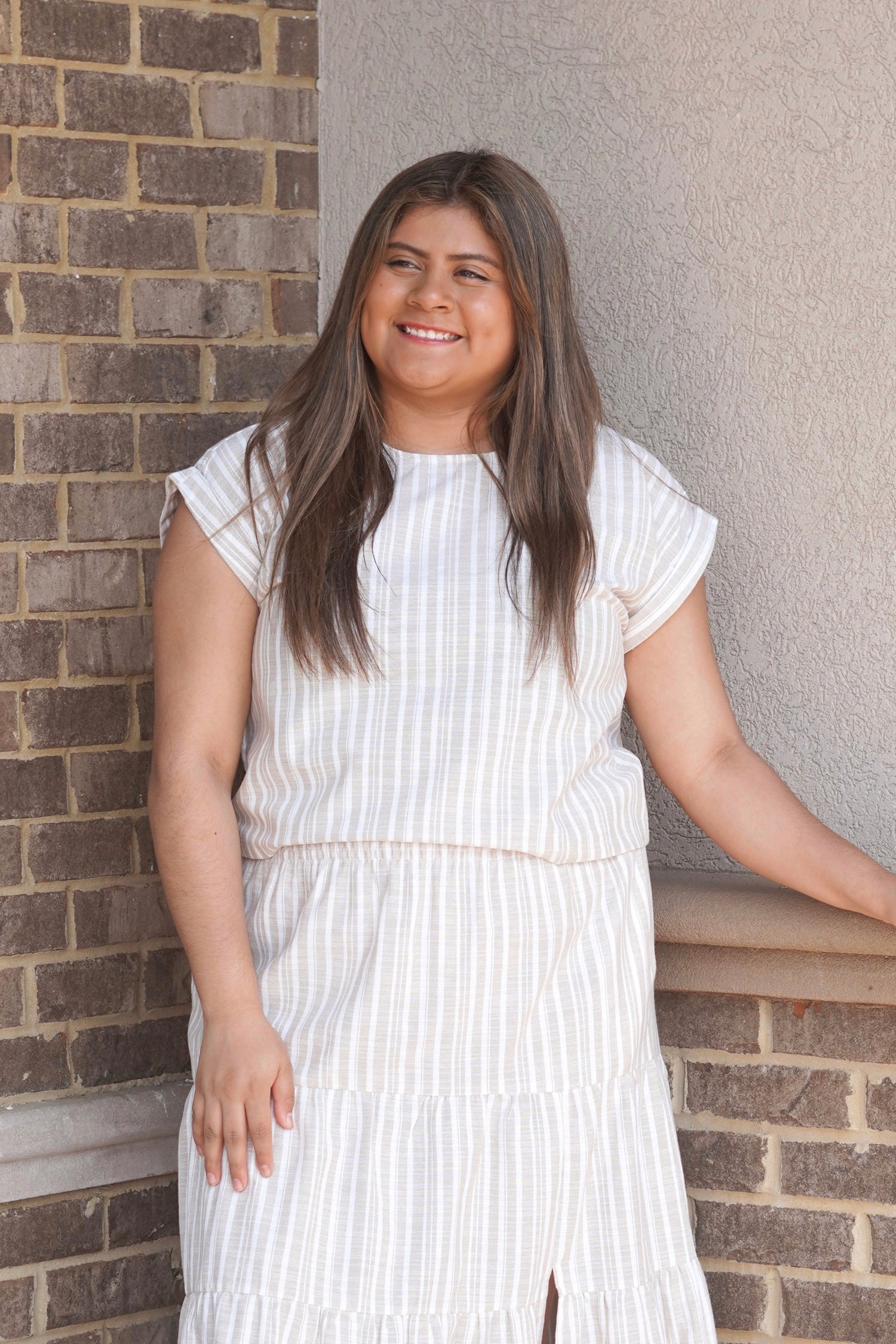Women wearing a taupe and white striped top, short sleeve, scoop neckline paired with the matching skirt. 