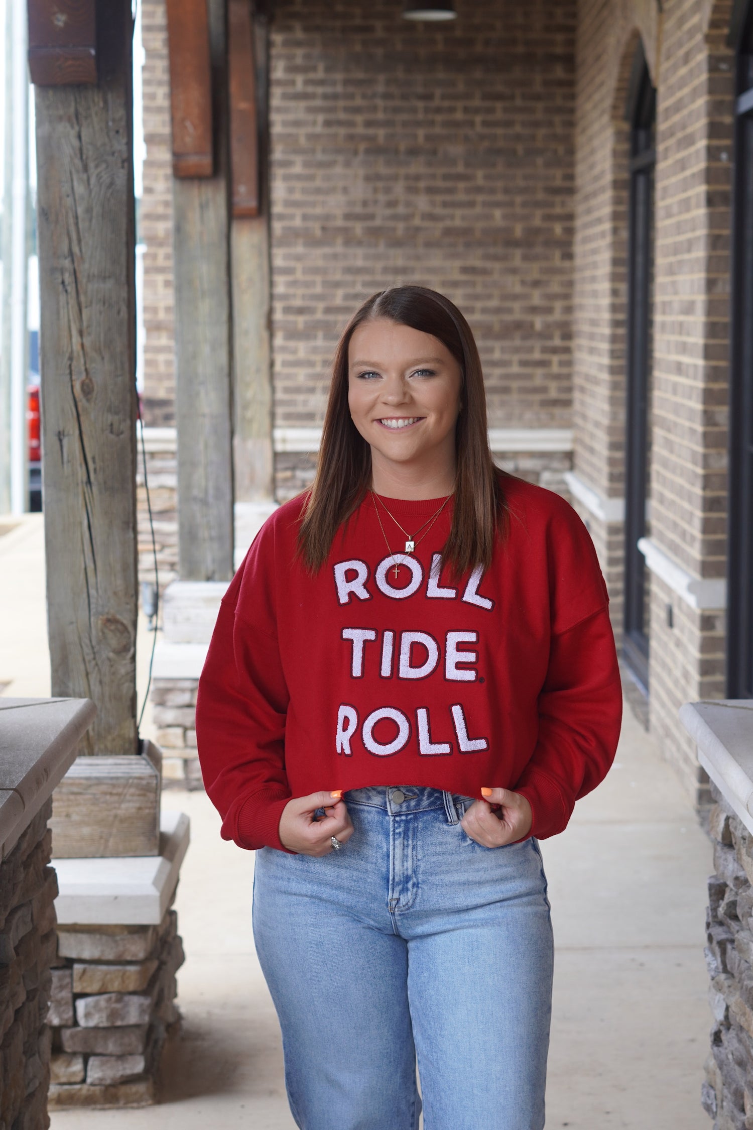 Woman wearing cropped red sweatshirt that says "roll tide roll"