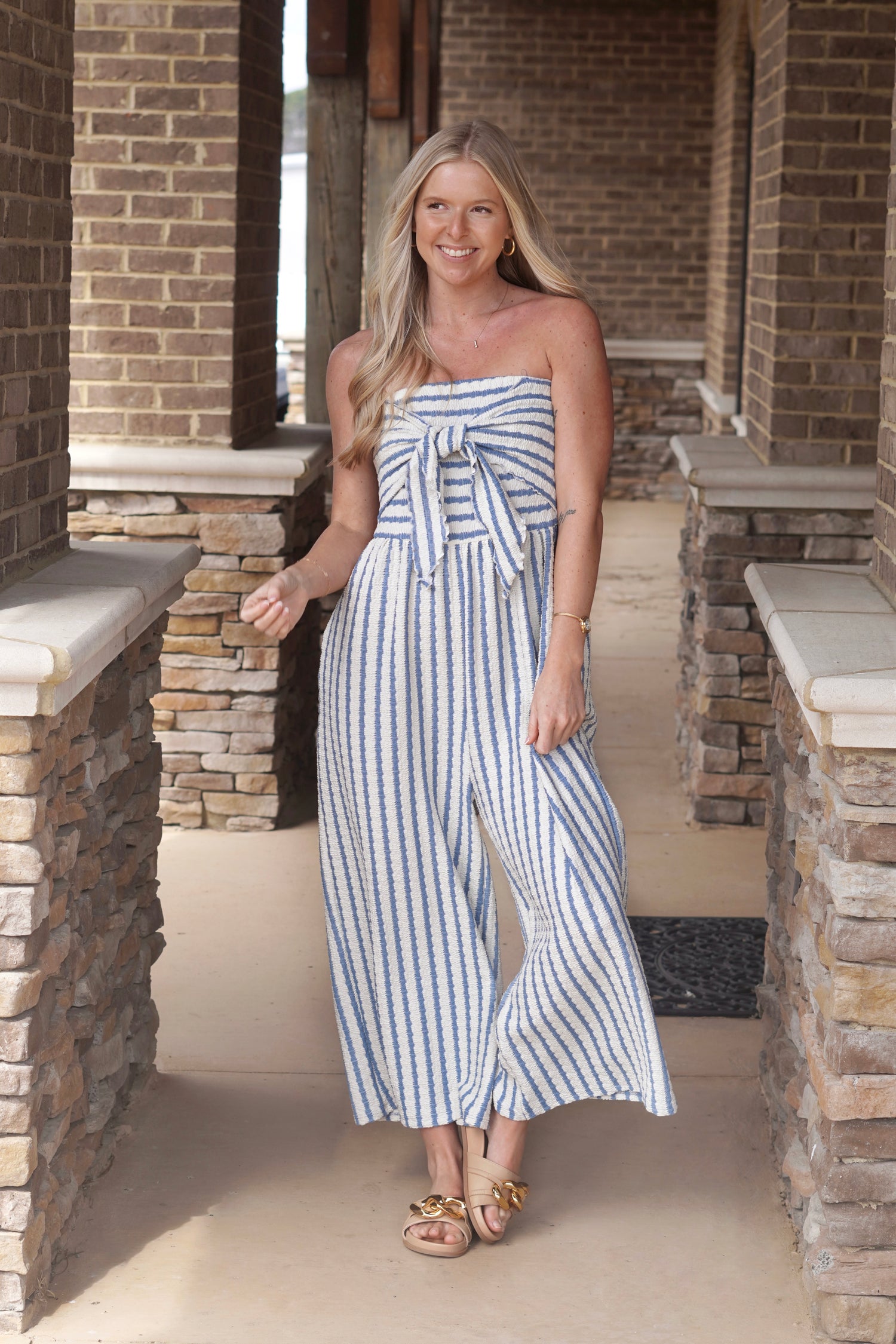 Woman wearing a blue and white vertically striped, textured, jumpsuit with a bow on the front