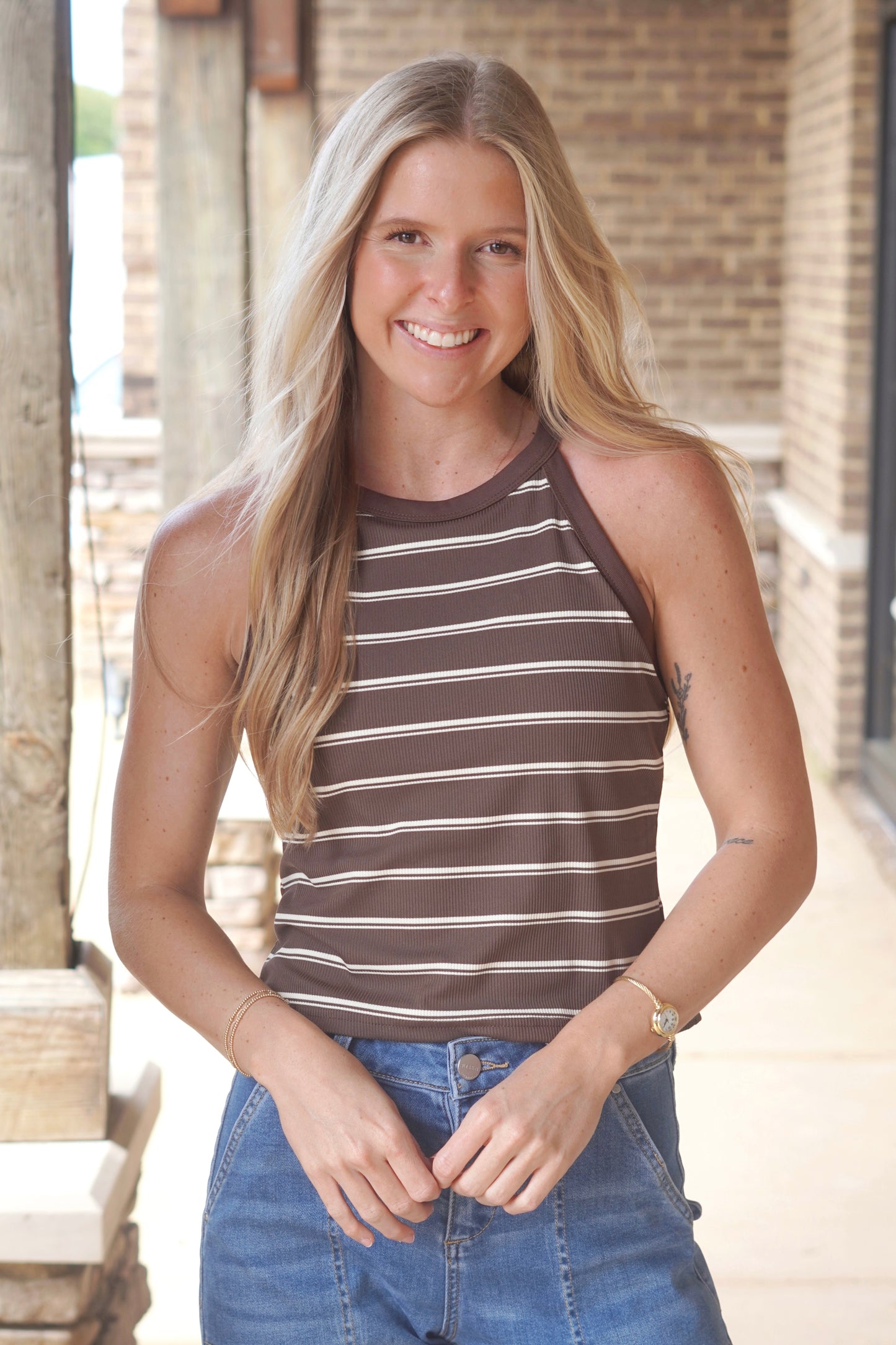 Women wearing an brown top with white stripes, high neck, sleeveless. 