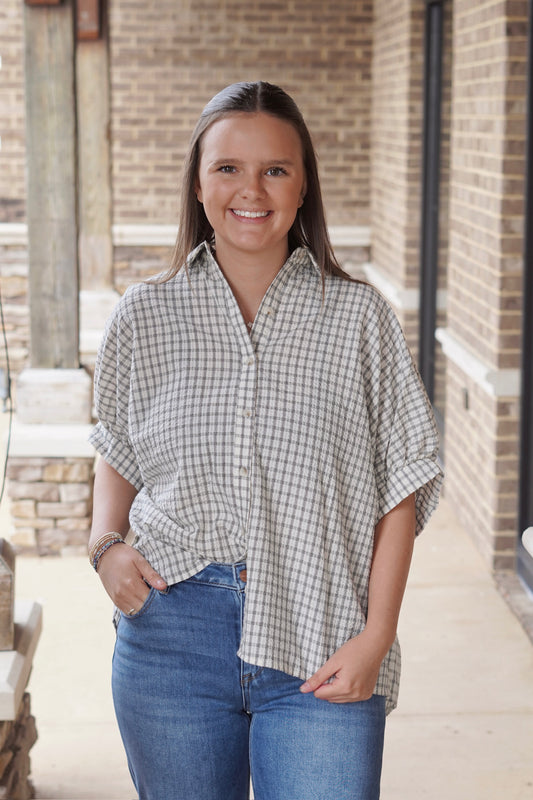 Woman wearing a black and white short sleeve gingham button down top paired with denim jeans